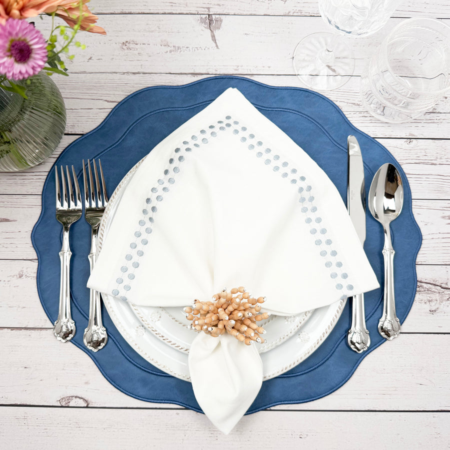 Blue placemat with a white gray-dot embroidered napkin and wood bead napkin ring on whitewashed wood