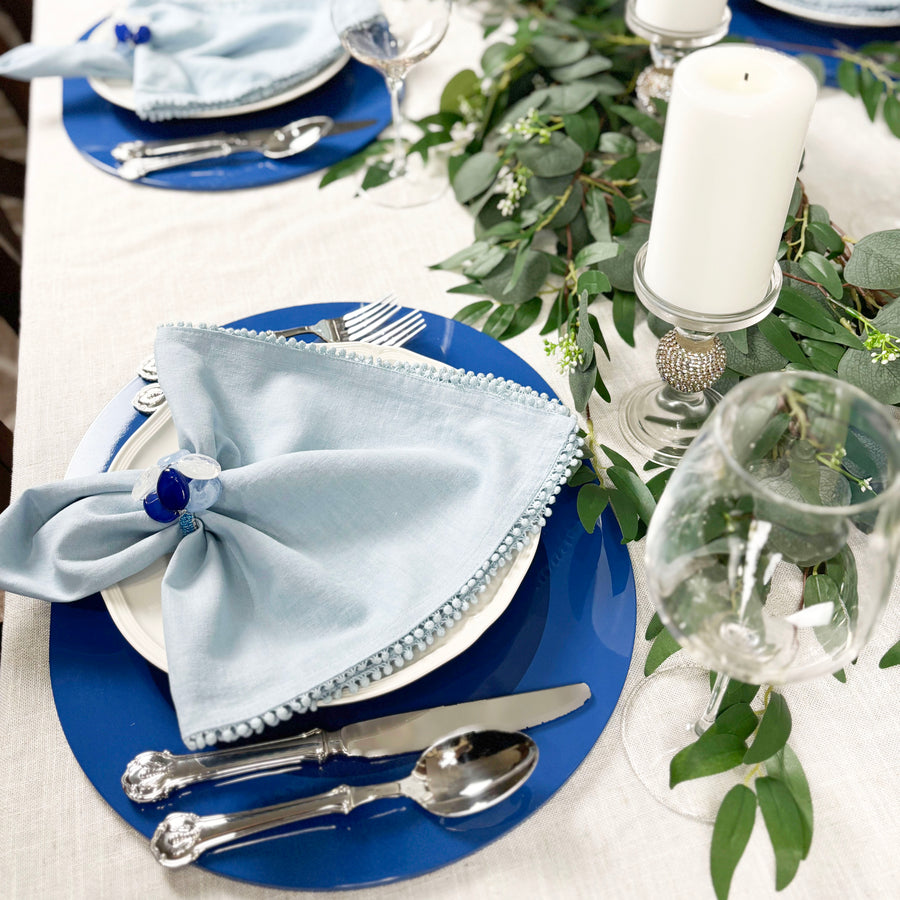 Blue Kelly lacquered wood placemat with a light blue napkin, candles and eucalyptus