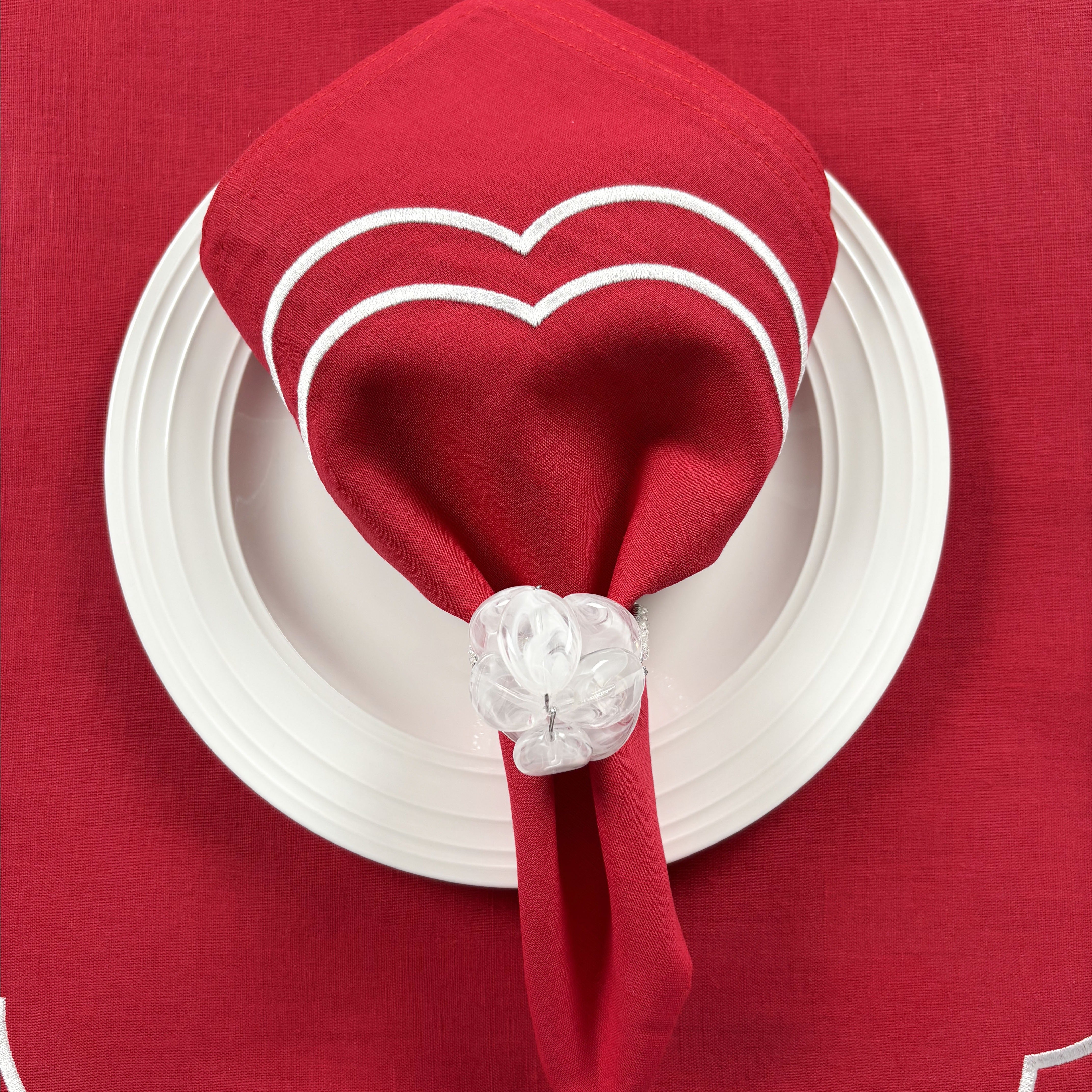 Christmas Table Set for 4 (Red): red Charlotte napkin with white scallop embroidery folded on a white plate, held by a white beaded Pebble Stone napkin ring, on a red Charlotte placemat