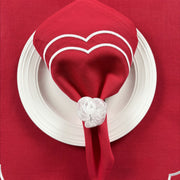 Christmas Table Set for 4 (Red): red Charlotte napkin with white scallop embroidery folded on a white plate, held by a white beaded Pebble Stone napkin ring, on a red Charlotte placemat